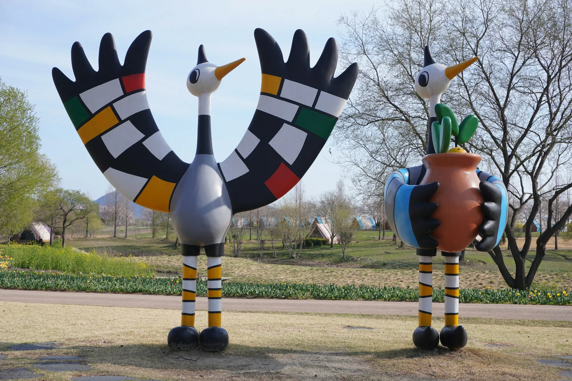 Two brightly coloured bird sculptures standing in a park