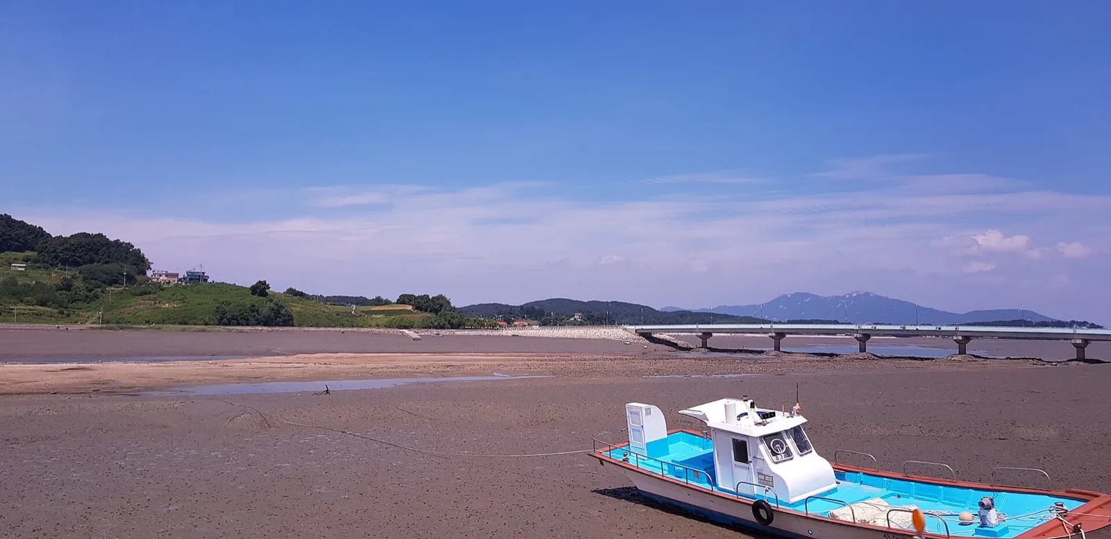 A wide mudflat at low tide on Sido, with a small fishing boat resting on the mud and a bridge across the water on the right