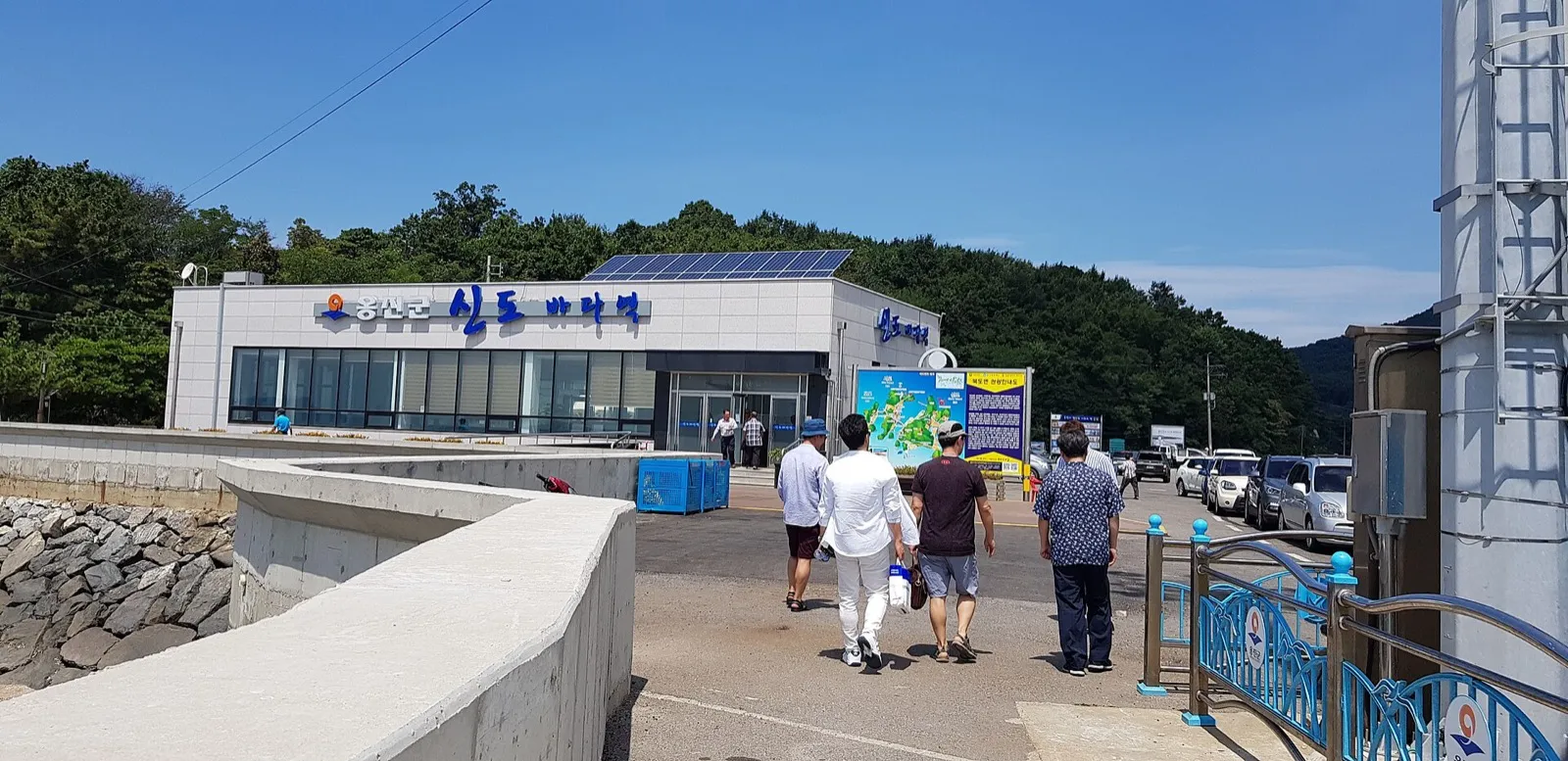A low terminal building with a sign reading 옹진군 신도바다역, beside a car park by the sea