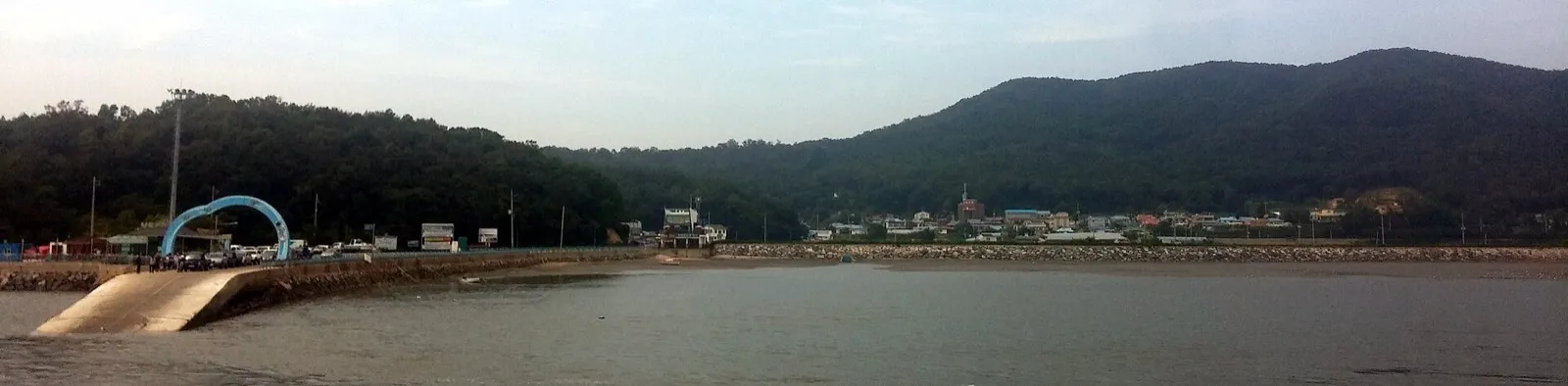 A wide panorama of the Sindo wharf and Gonam village, with the sea in front and low hills behind